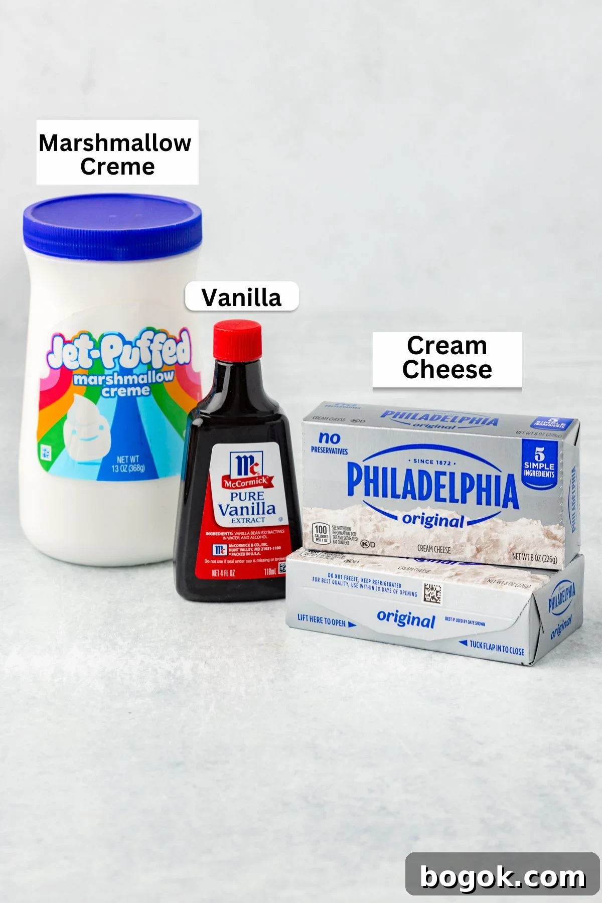 A jar of Jet-Puffed marshmallow creme, a bottle of McCormick pure vanilla extract, and a box of Philadelphia original cream cheese are arranged on a light surface—classic ingredients for Marshmallow Fruit Dip. Each item is clearly labeled.