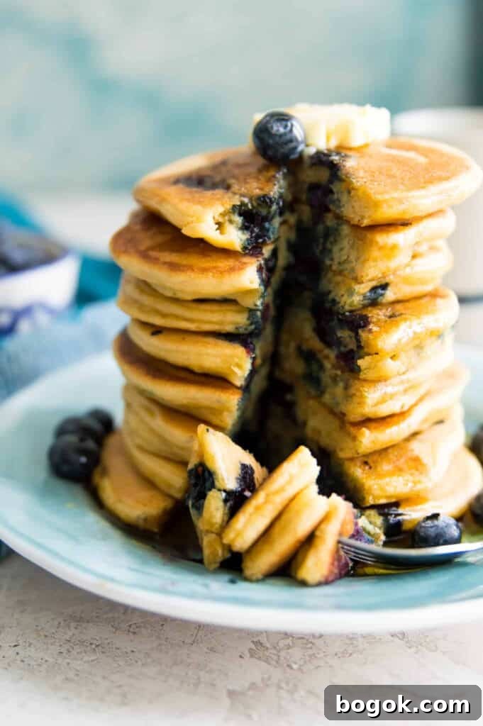 Fluffy Paleo Blueberry Pancakes: Grain-Free Breakfast Recipe 8 A stack of blueberry pancakes on a plate with a slice taken out of them.