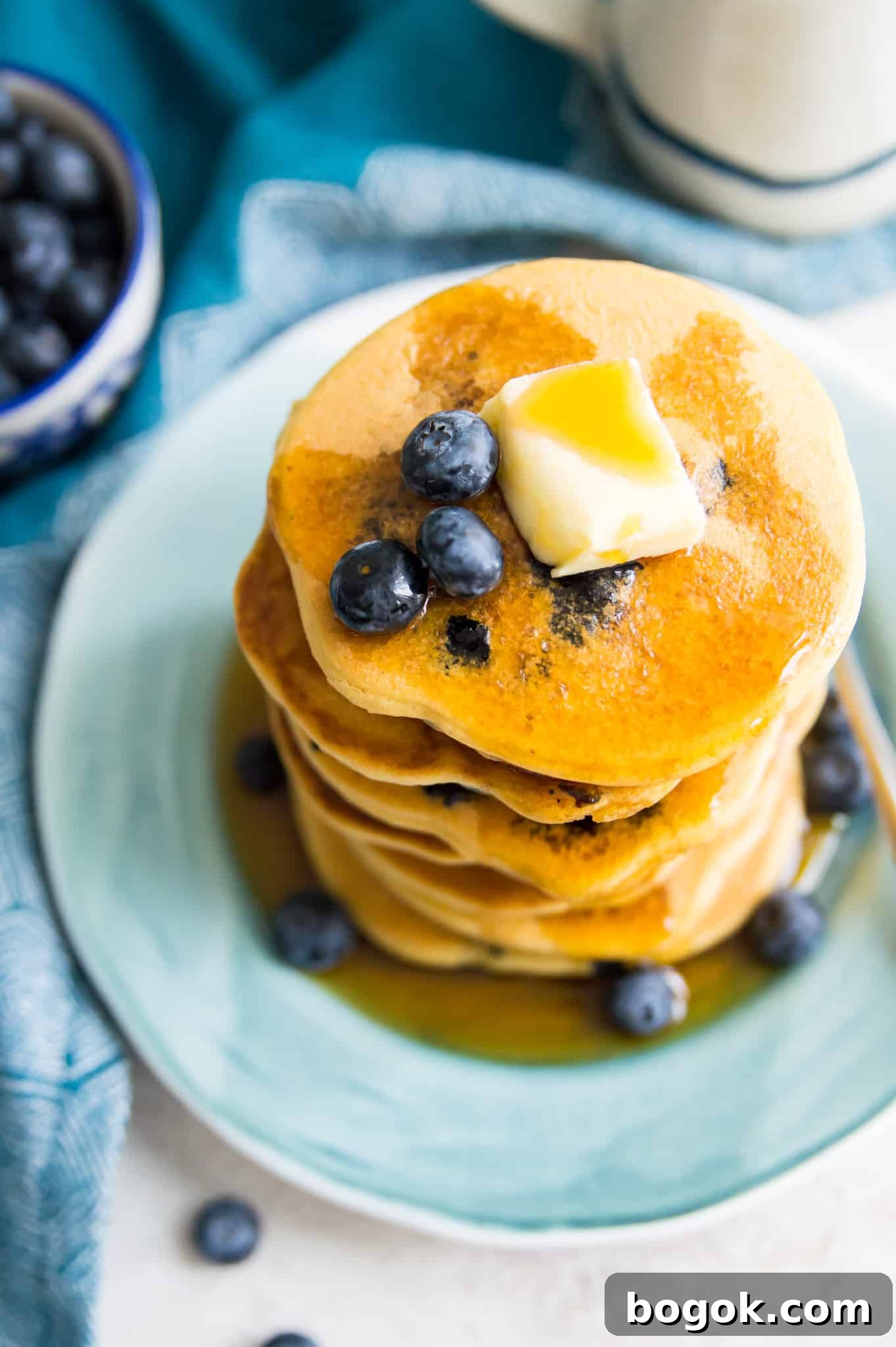 Fluffy Paleo Blueberry Pancakes: Grain-Free Breakfast Recipe 9 A stack of blueberry pancakes on a plate with syrup and butter on top.