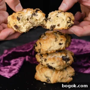 Holding a rock cake which is broken in half by hand with three rock cakes stacked up in the background