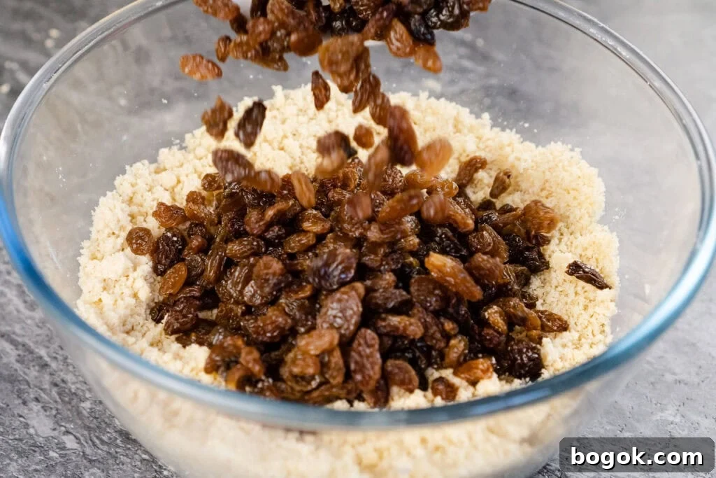 sultanas added into flour and butter cake mix in a glass bowl