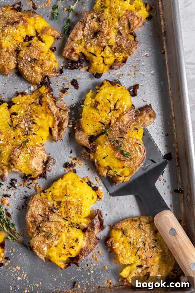 A spatula lifting a crispy smashed potato from a baking sheet.