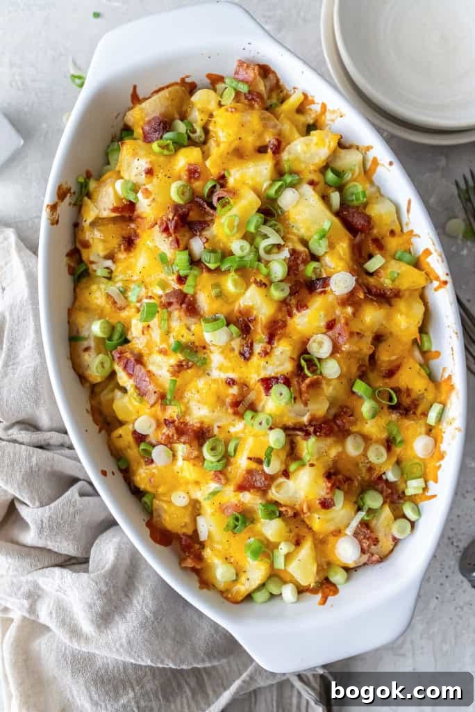 Twice Baked Potato Casserole in a white baking dish topped with melted cheddar, crisp bacon, and green onions.