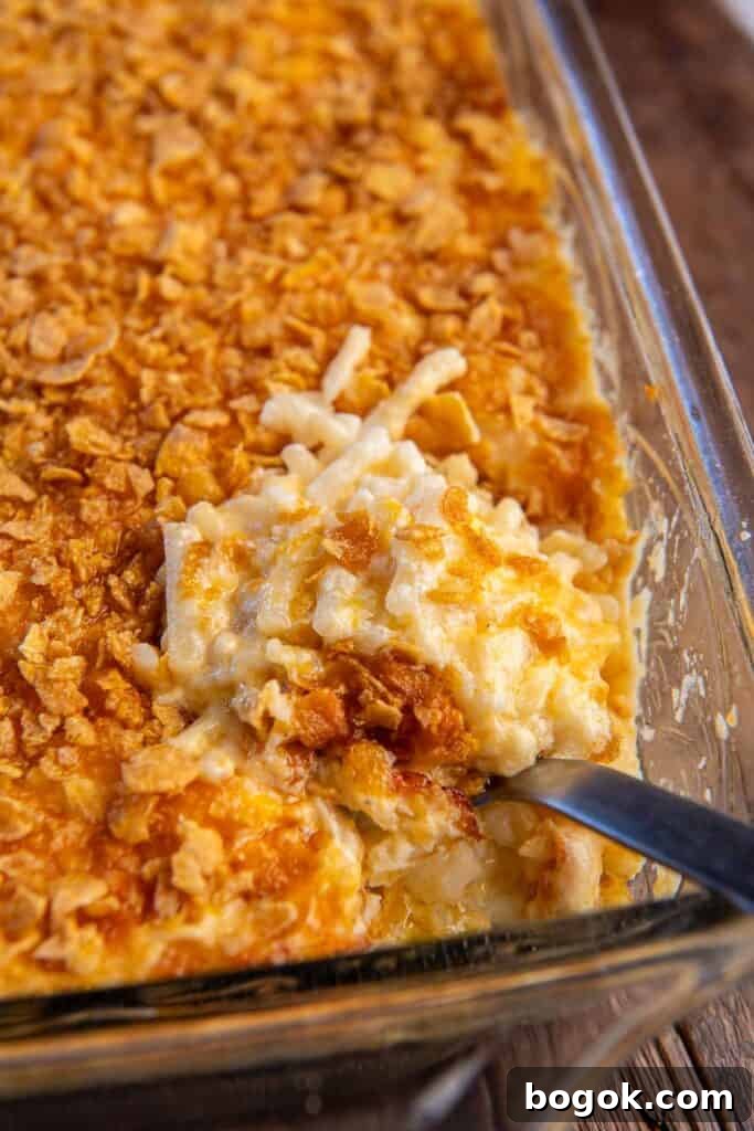 Cheesy hash brown casserole being scooped with a spoon.