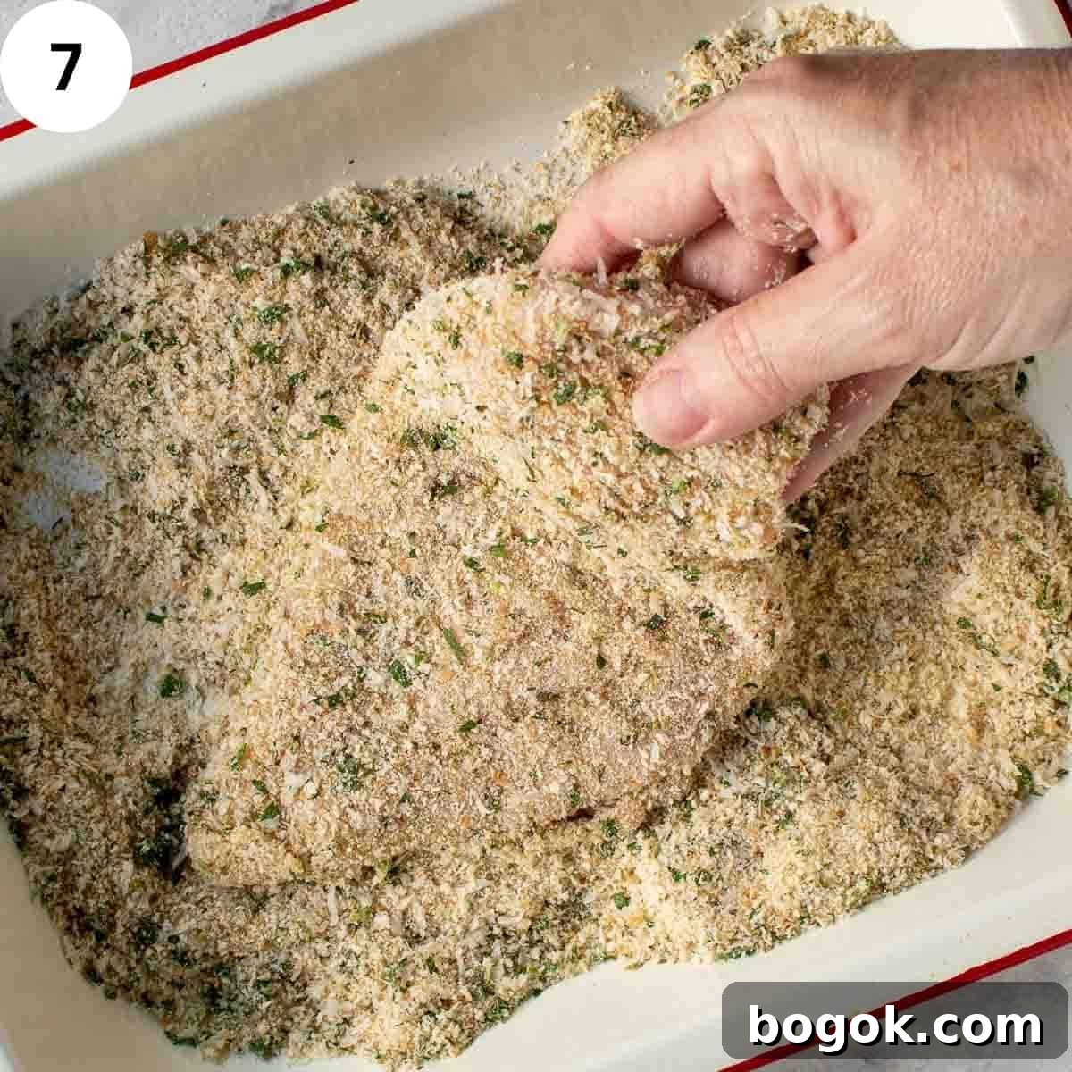 Uncooked chicken breast covered with breadcrumbs.