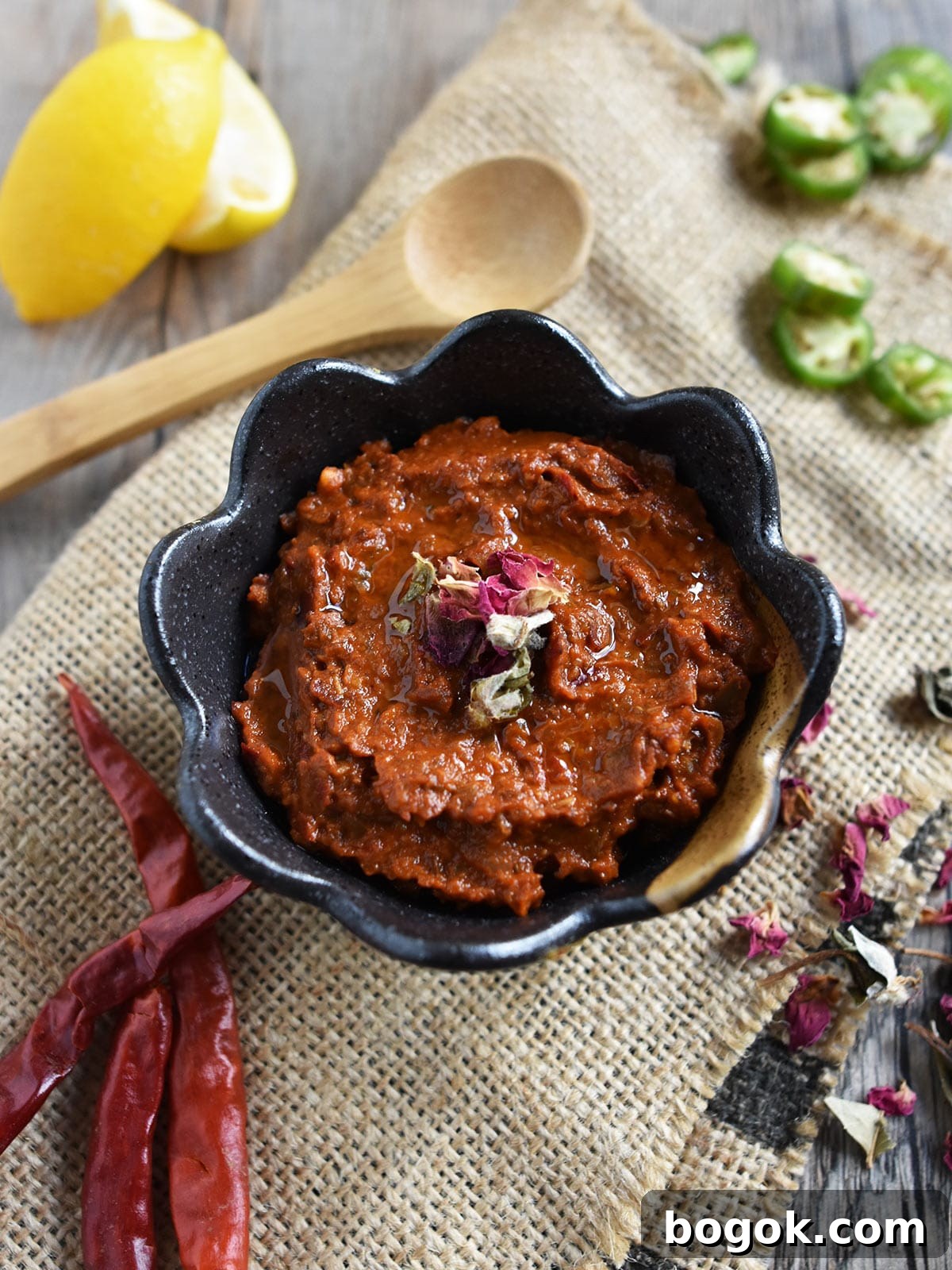 Smoky Rose Harissa: Spicy Condiment with Floral Notes 2 Rose harissa in brown bowl on burlap with peppers, lemon and rose petals.