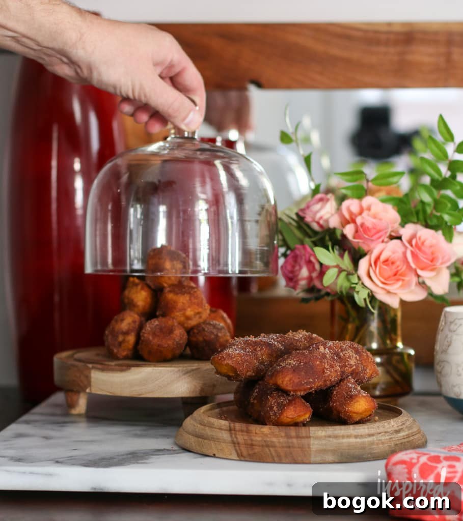 baked pumpkin donuts on wood stands with a hand lifting up a glass cloche.