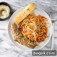 A serving of one pot spaghetti and sausages with a crispy topping and Parmesan cheese on the side.