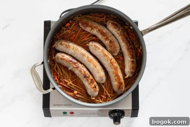Adding water, dry spaghetti, and sausages to the pan to make the one pot spaghetti and sausage meal.