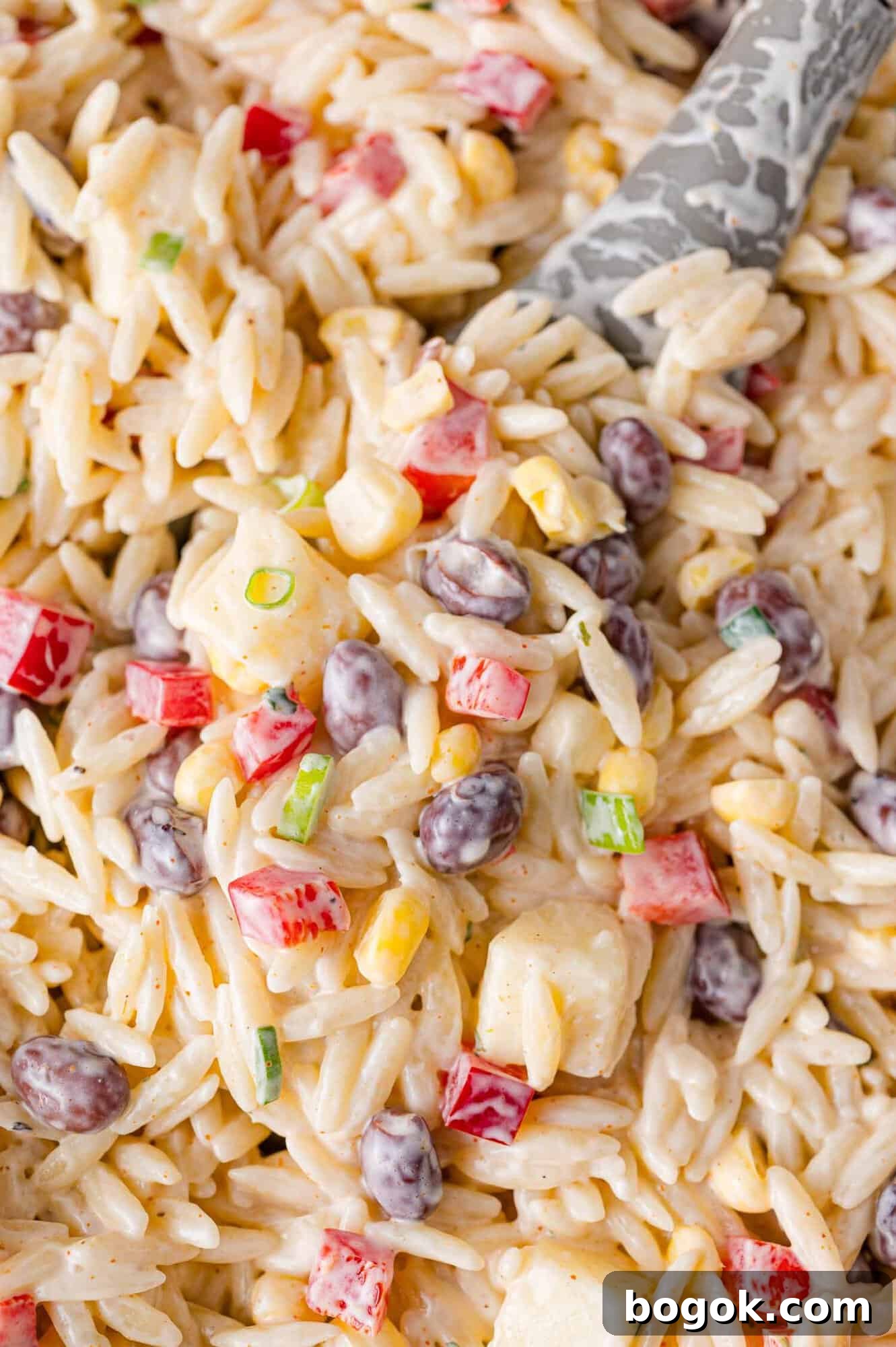 Creamy southwestern orzo salad on a serving spoon and in a large bowl.