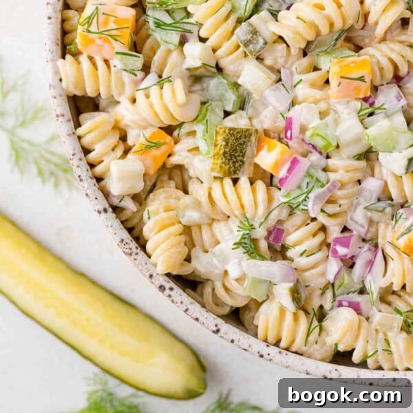 Dill pickle pasta salad with rotini pasta, in a bowl, with a dill pickle next to it.