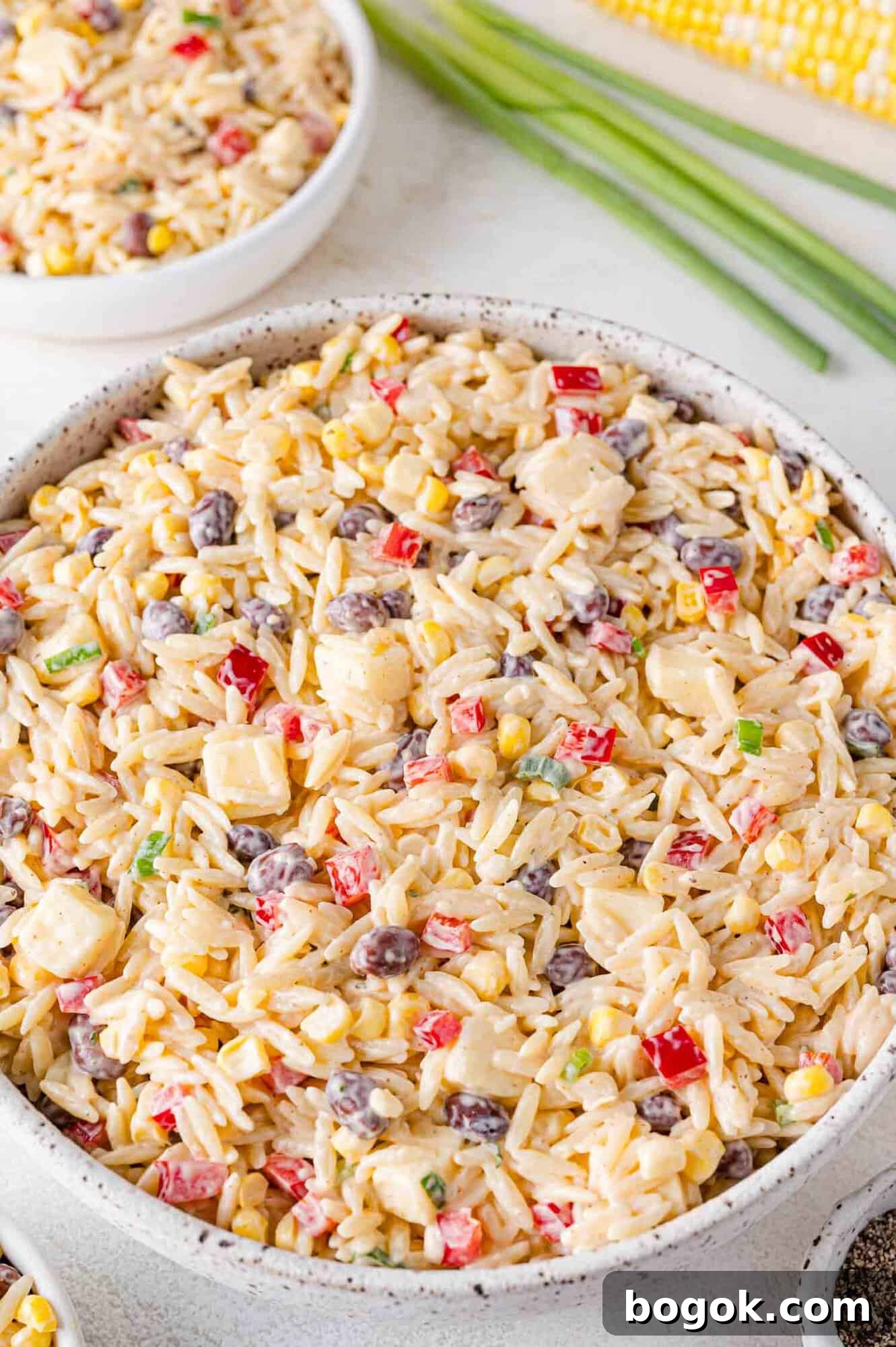 Orzo salad with black beans, corn, red bell peppers, and cheddar cheese, in a large bowl.