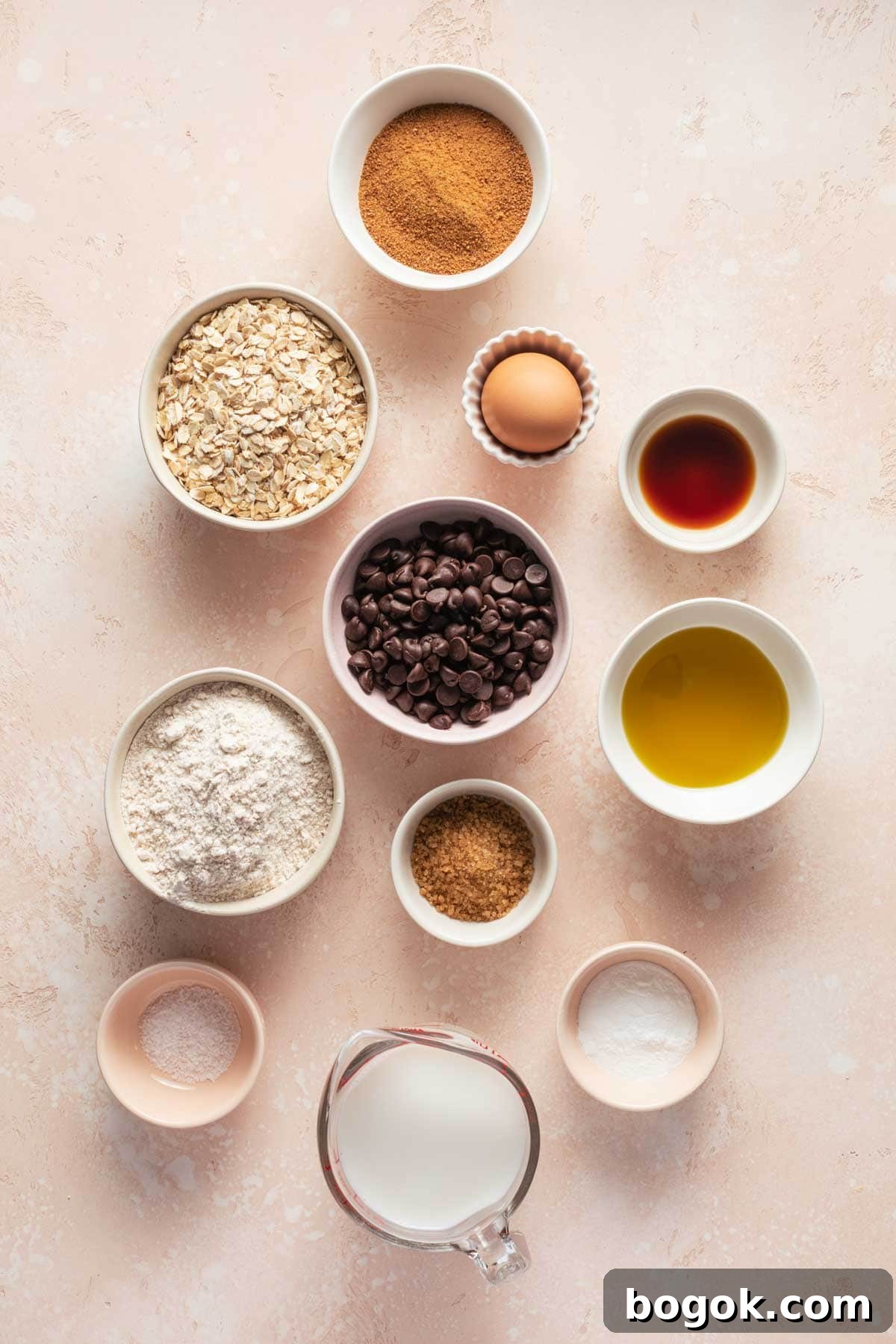 Ingredients to make air fryer muffins arranged in individual dishes on a pink surface.