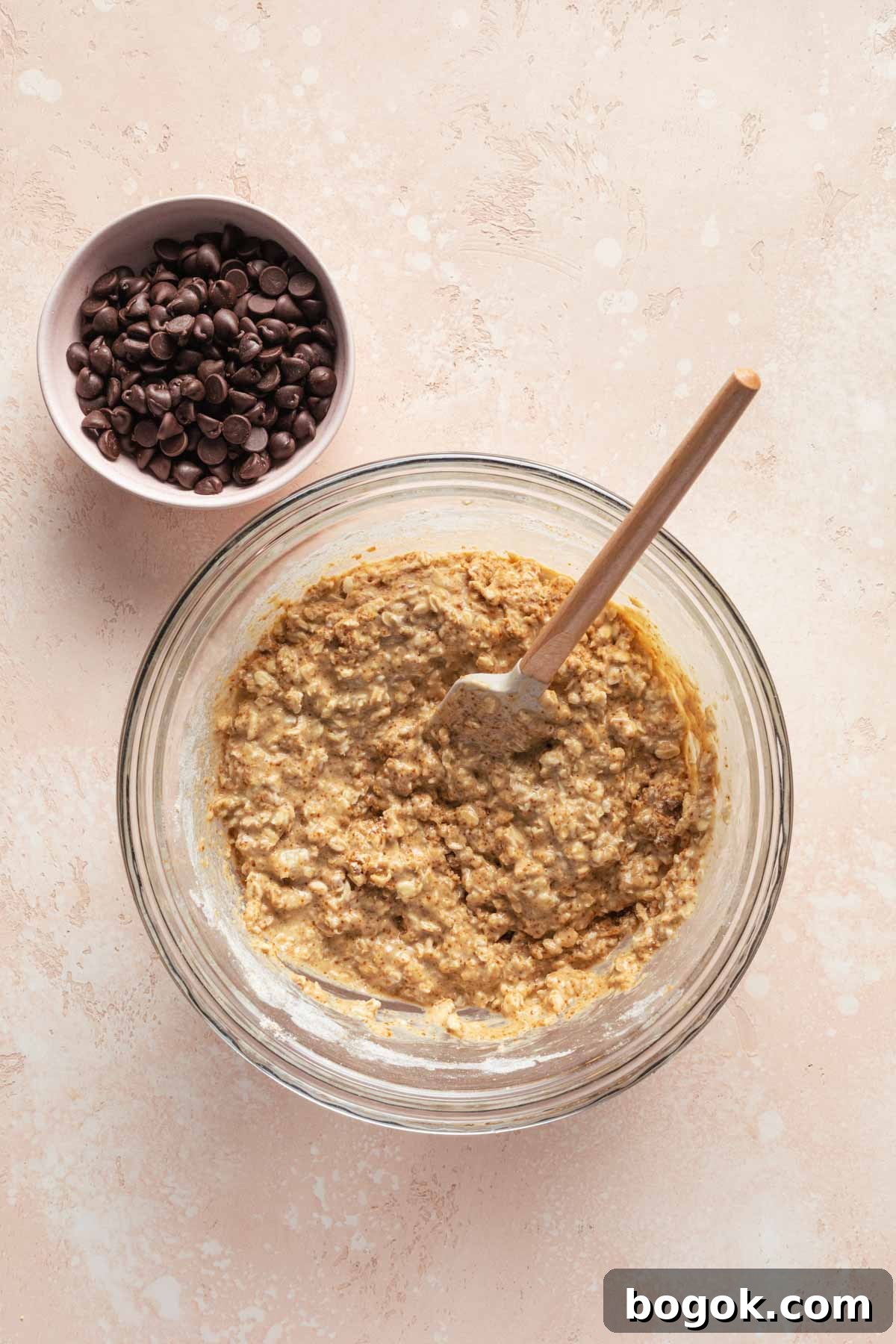 Oatmeal muffin batter in a glass bowl with a spatula inserted into it.