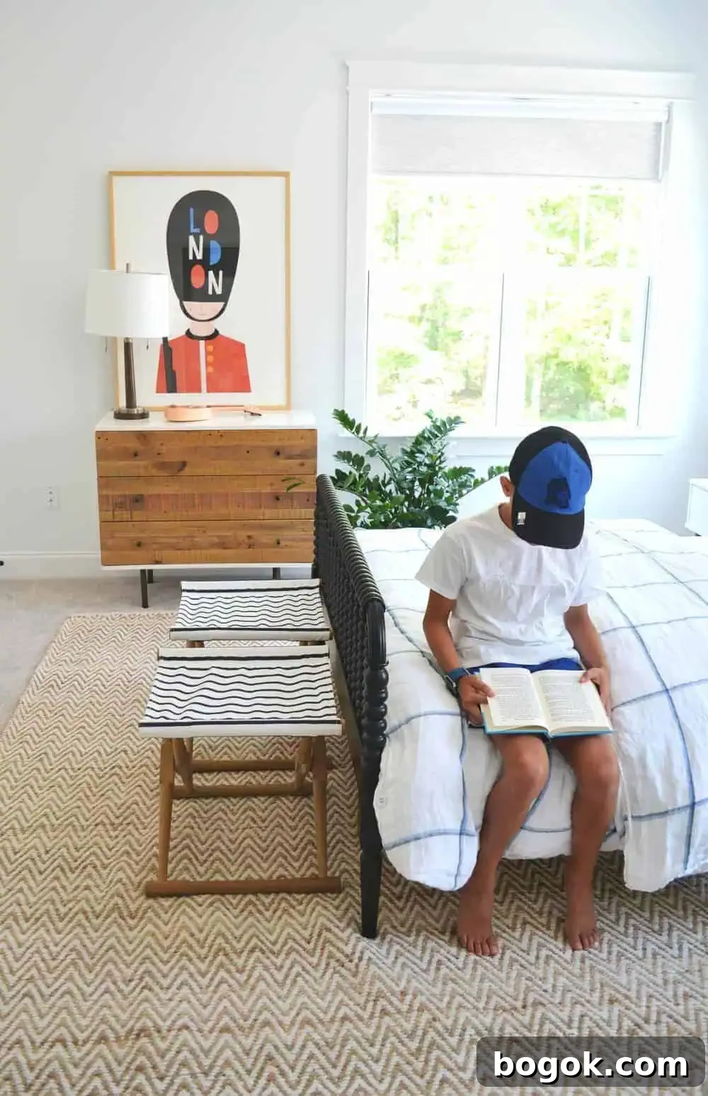 a kids bedroom and a boy sitting on the bed reading with a piece of oversized art on the wall