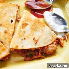 BBQ chicken quesadillas on plate with spoons of barbecue sauce and sour cream.