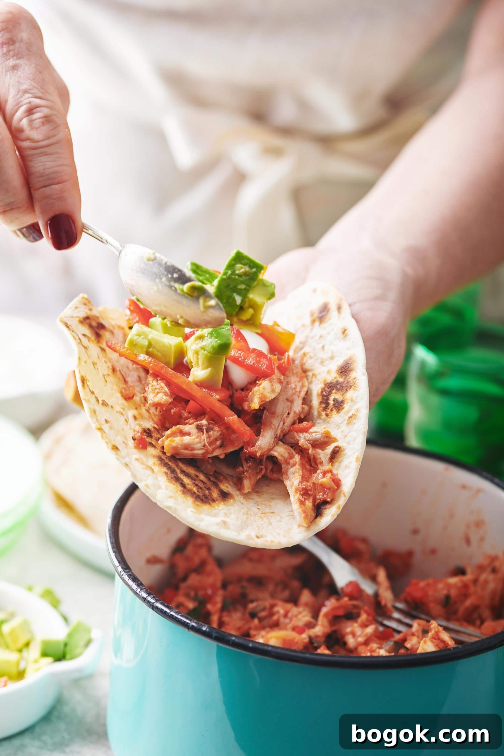 Spoon scooping avocado onto a Shredded Chicken Taco.