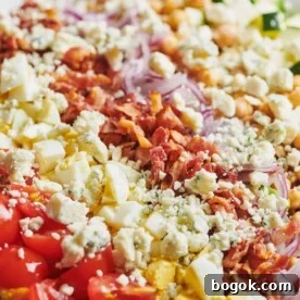Late Summer Cobb Salad topped with bacon, red onion, crumbled cheese, and other toppings.