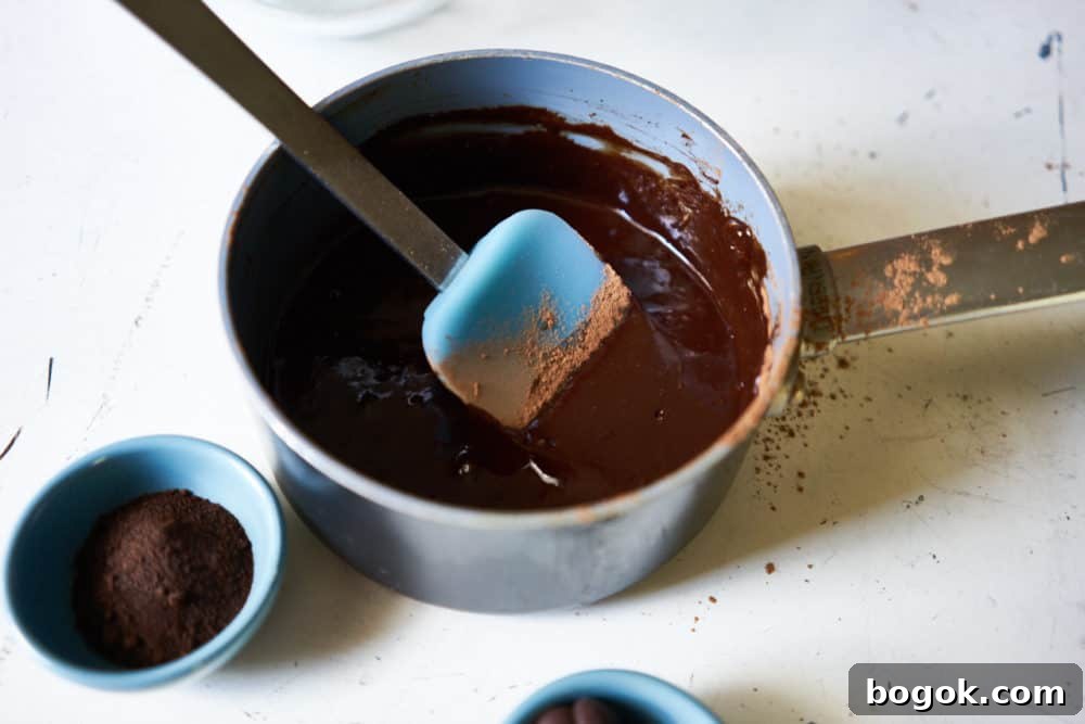 A small sauce pan with melted chocolate and a blue spatula.