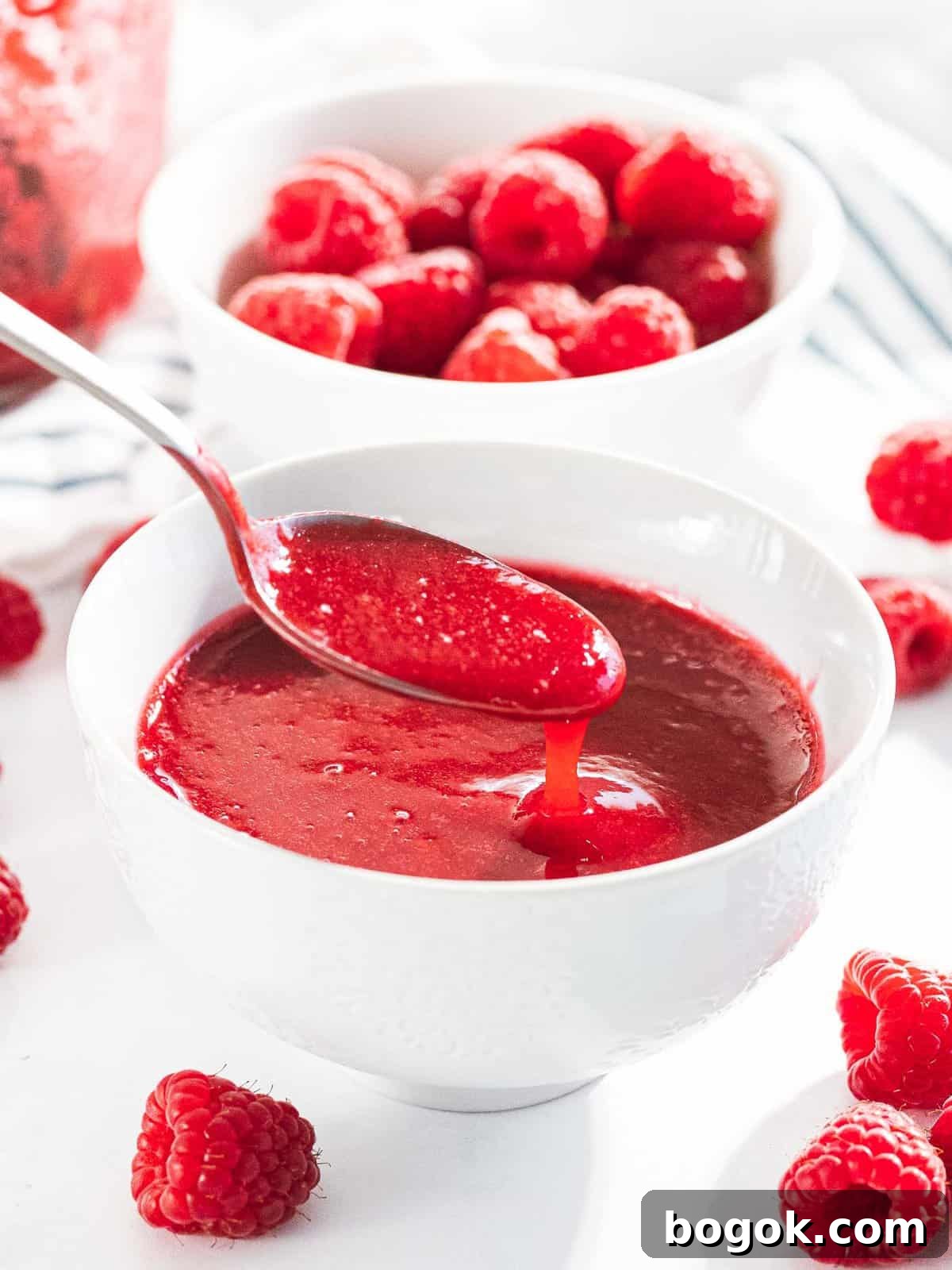 Raspberry sauce or raspberry coulis drizzled off a spoon into a bowl.
