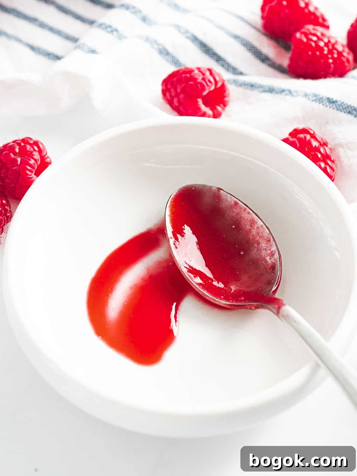 Raspberry sauce drizzled on a plate with a spoon running through it to show the thickness.