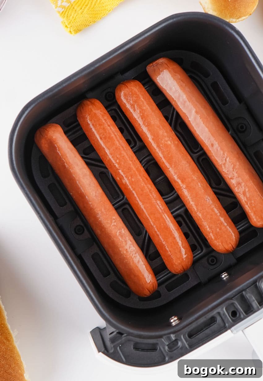 four uncooked hot dogs arranged in a row in the basket of an air fryer