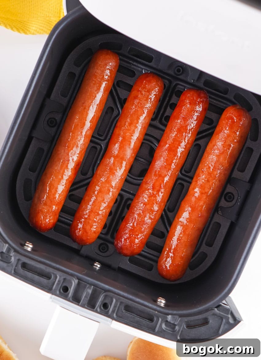 four cooked hot dogs arranged in a row in the basket of an air fryer