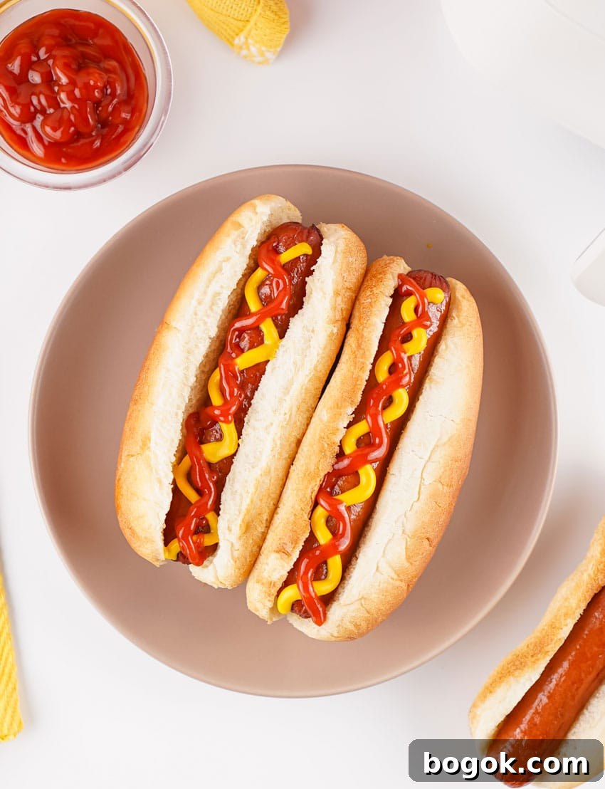 two air fryer hot dogs topped with ketchup and mustard in fluffy buns on a gray plate