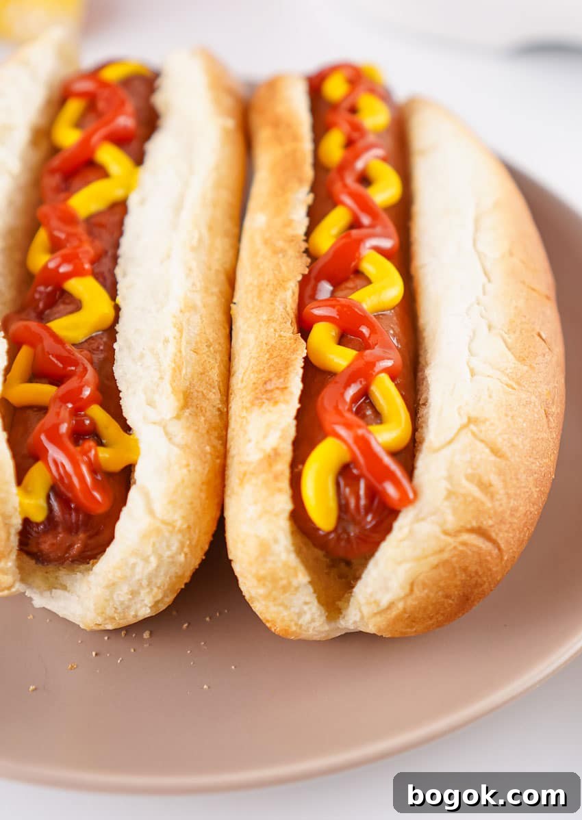 two air fryer hot dogs topped with ketchup and mustard in fluffy buns on a gray plate