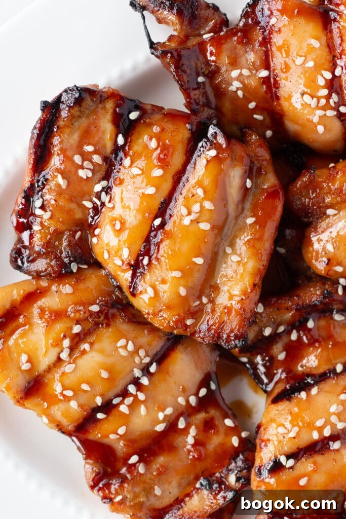 Close up of grilled boneless skinless chicken thighs with a soy honey glaze and white sesame seeds sprinkled on top, all on a white platter.