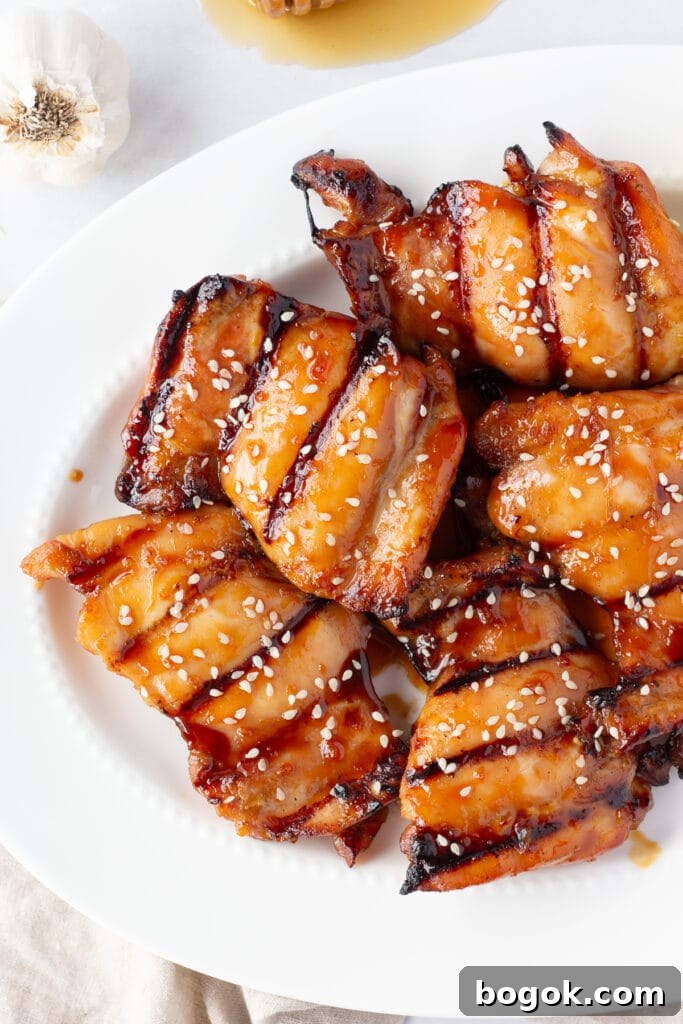 Top down shot of grilled boneless skinless chicken thighs with a soy sauce glaze and white sesame seeds on them on a white platter.