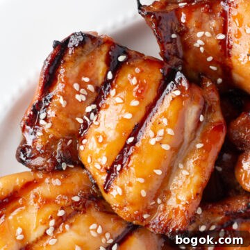 Close up of grilled boneless skinless chicken thighs with a soy honey glaze and white sesame seeds on a white platter.