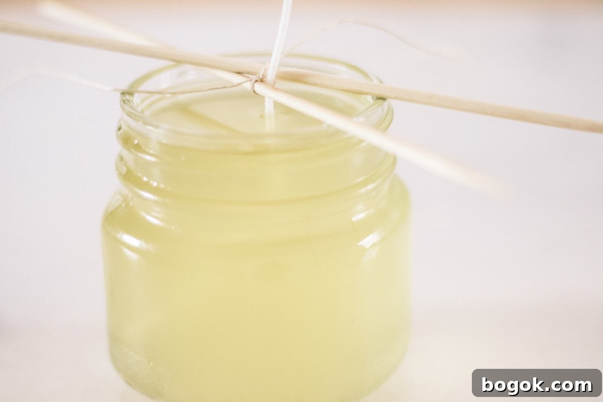 A jar of melted wax with a wick sticking out of it, wrapped around a stick to hold it up.