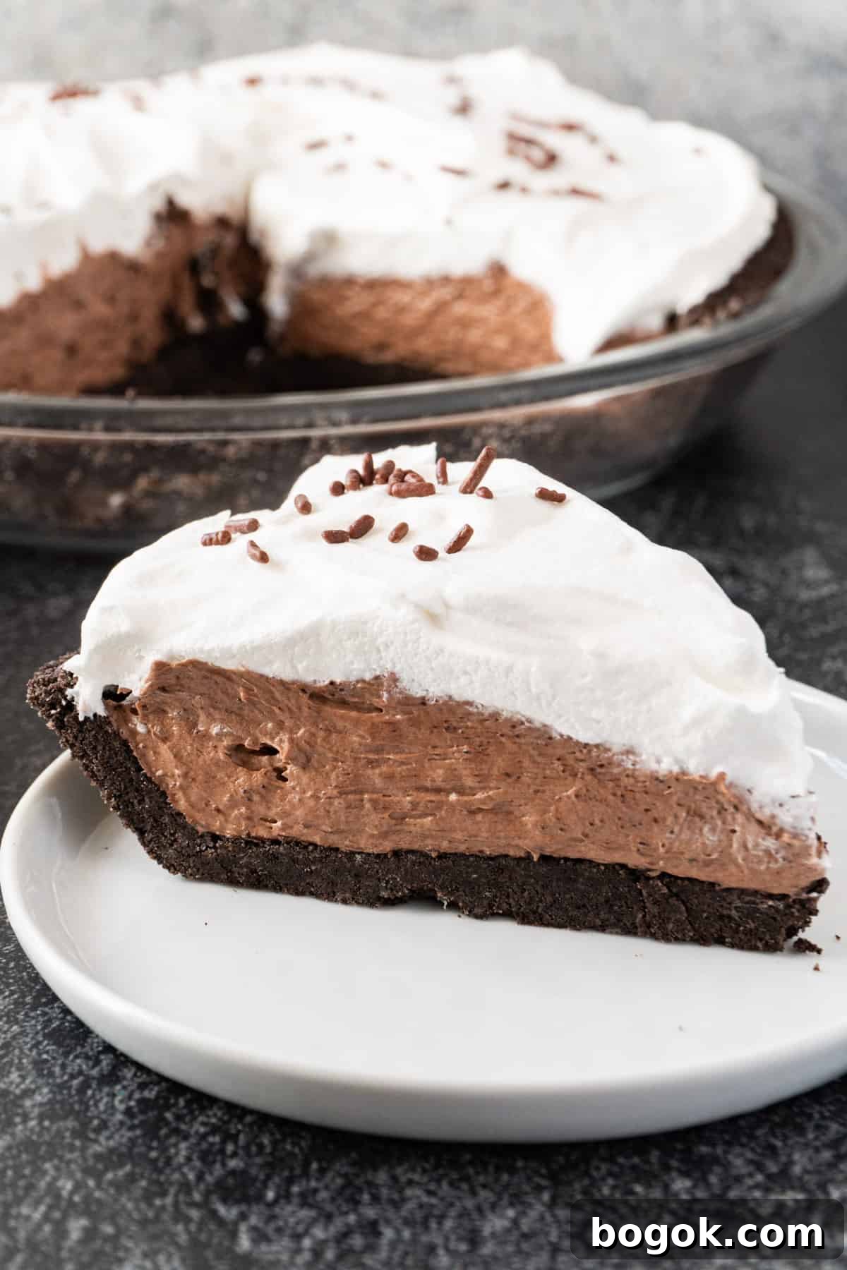chocolate pudding pie slice on white plate with rest of pie in background.