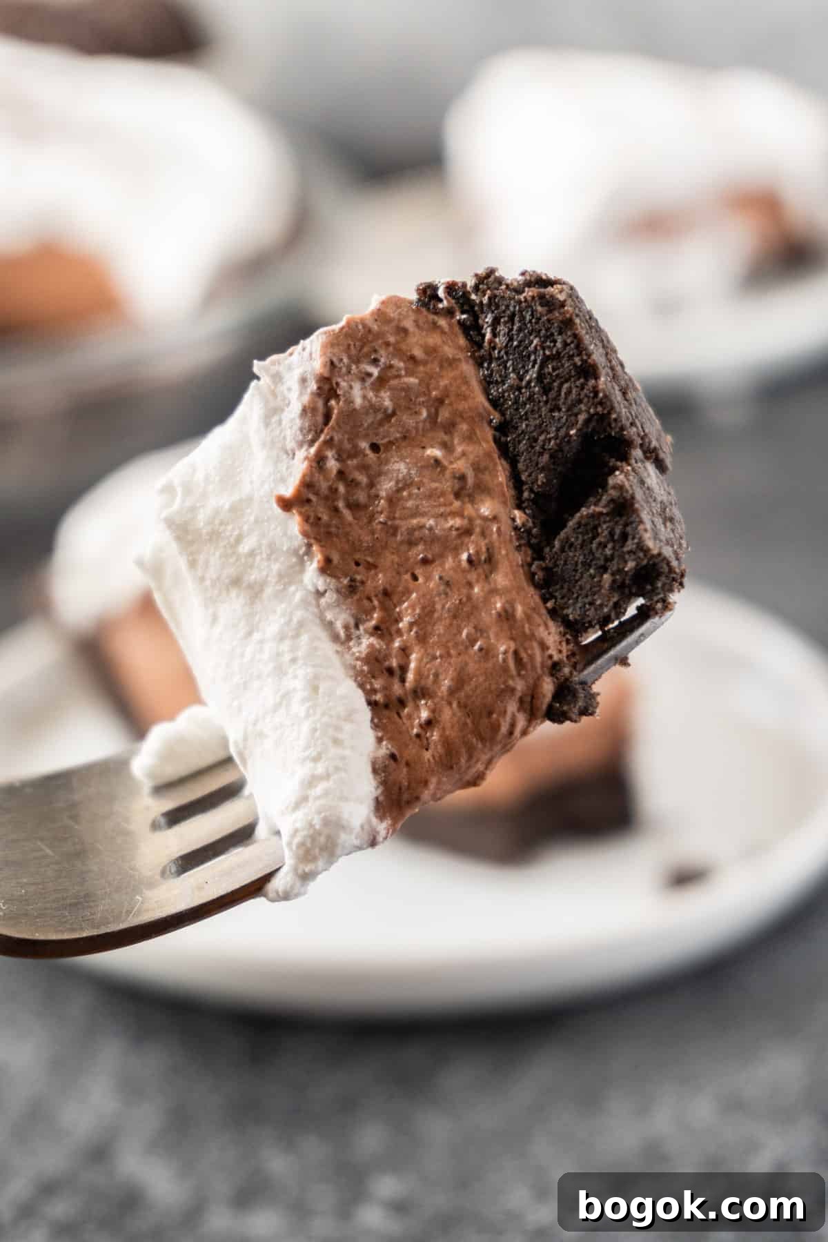 piece of chocolate pudding pie on a fork showing the three layers of Oreo crust, pudding filling, and whipped topping.