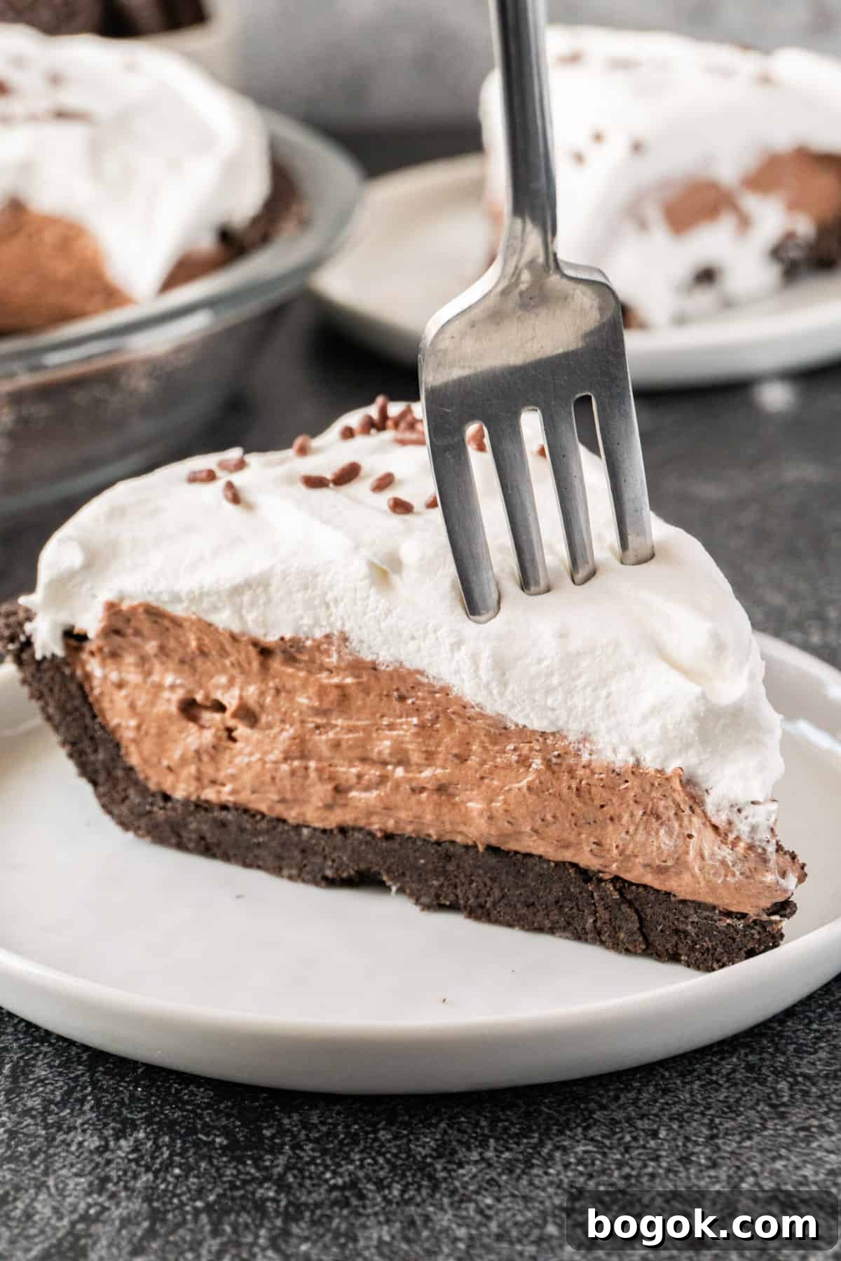 fork stuck into a slice of chocolate pudding pie, sitting on a white plate.
