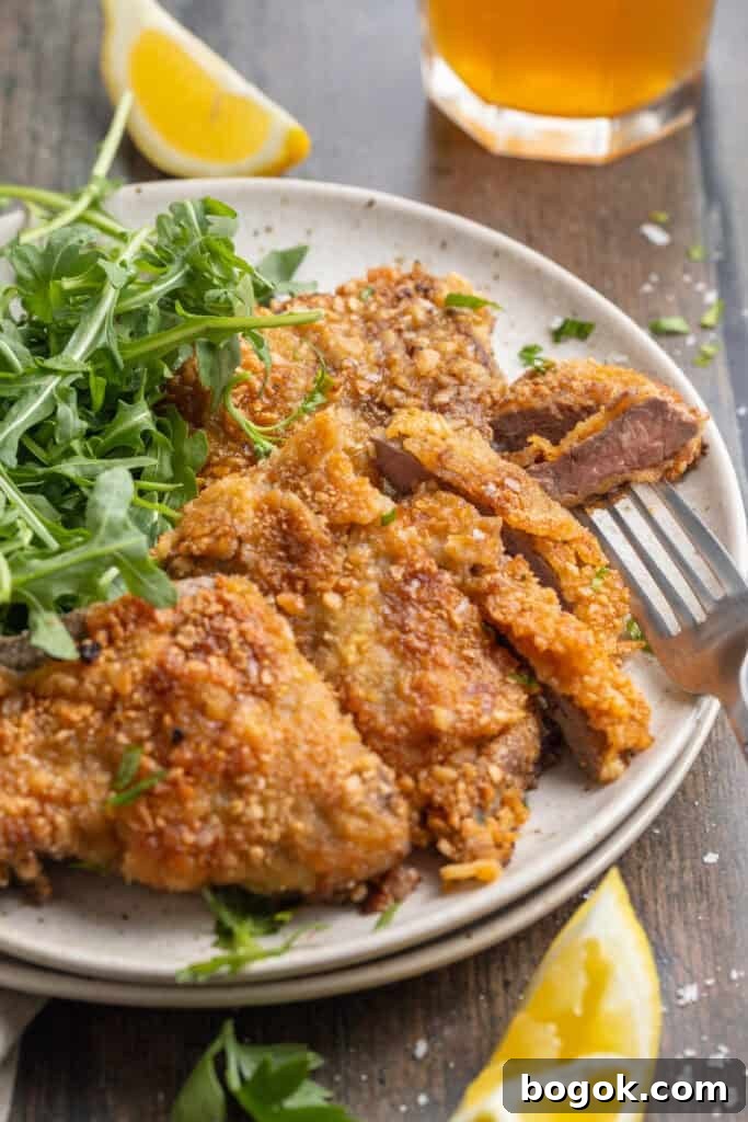 Overhead, angled, zoomed out view of crispy beef schnitzel plated with a salad of microgreens.