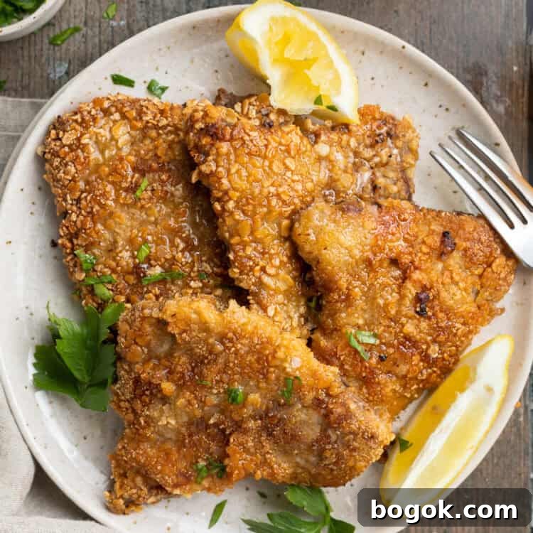 Overhead view of 4 crispy beef schnitzel steaks on a plate with microgreens and lemon wedges.