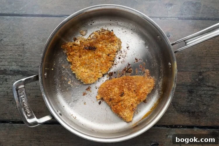 Overhead view of two breaded steaks in a pan with fry oil.