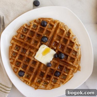 a whole wheat waffle on a white plate next to a fork