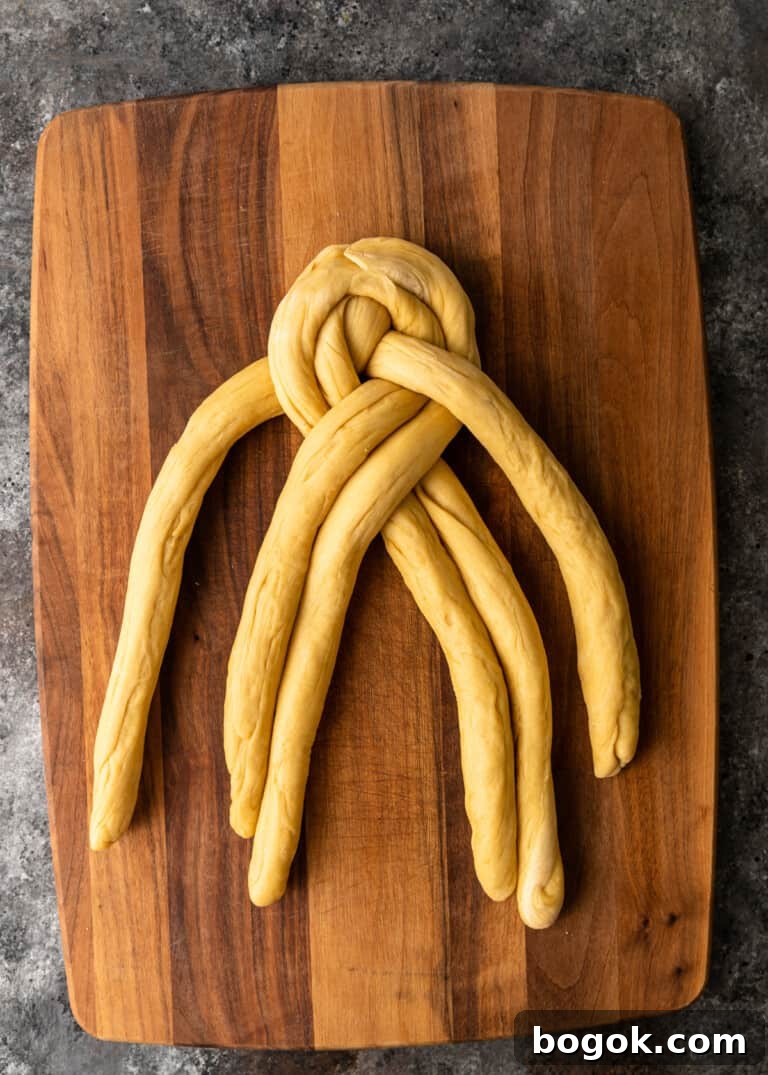 Authentic Challah Recipe: Soft, Braided Jewish Bread Tutorial 15 overhead process shot: dough rolled into six equal ropes tapered edges in the middle dough being braided on cutting board