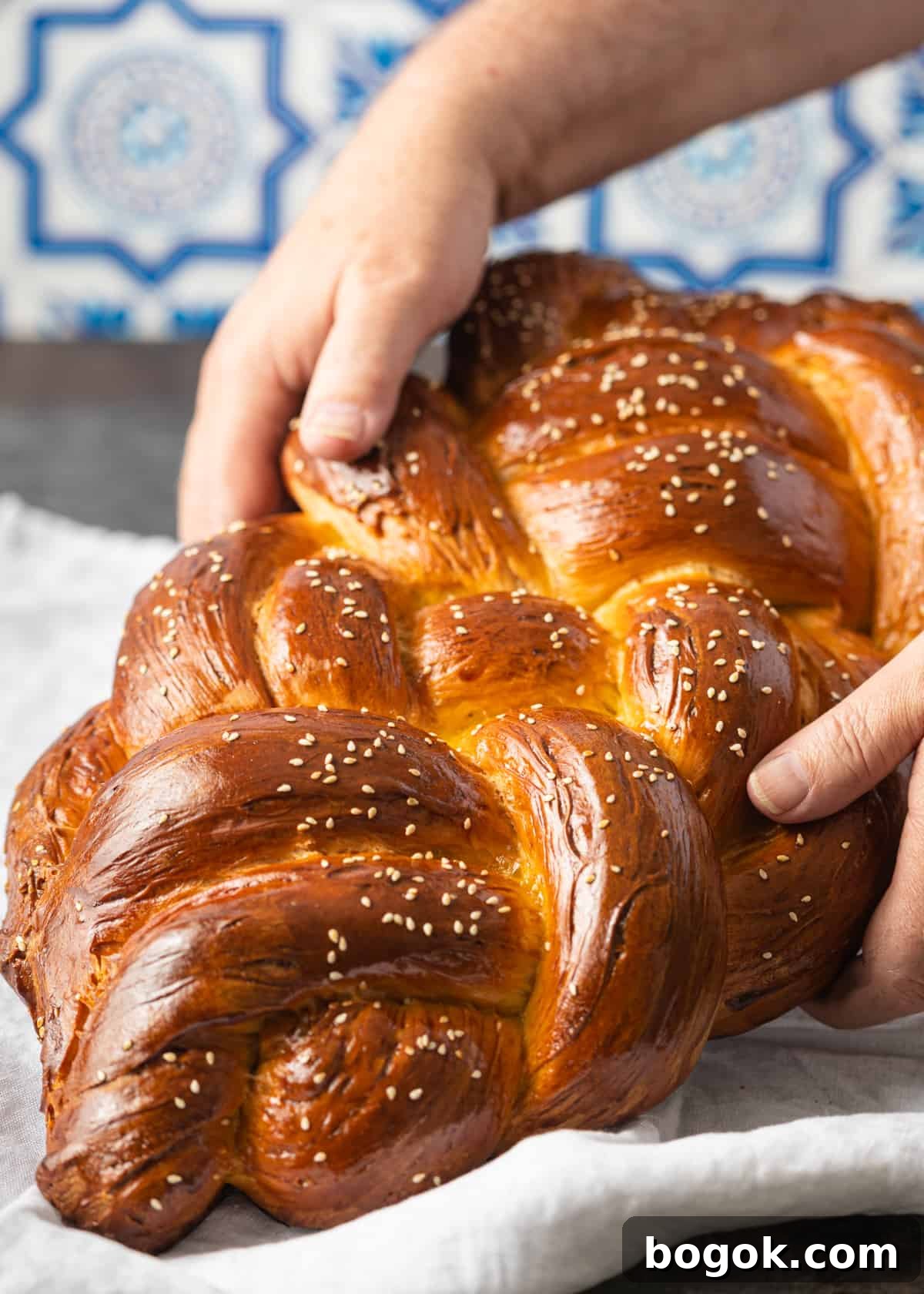 Authentic Challah Recipe: Soft, Braided Jewish Bread Tutorial 3 closeup view: hands holding challah lifted above tea towel