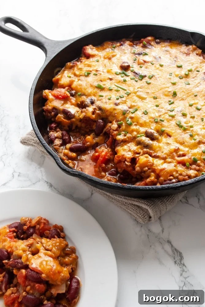 a skillet filled with lentil casserole that has a serving taken out of it next to a plate.