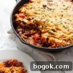 a skillet filled with lentil casserole that has a serving taken out of it next to a plate.