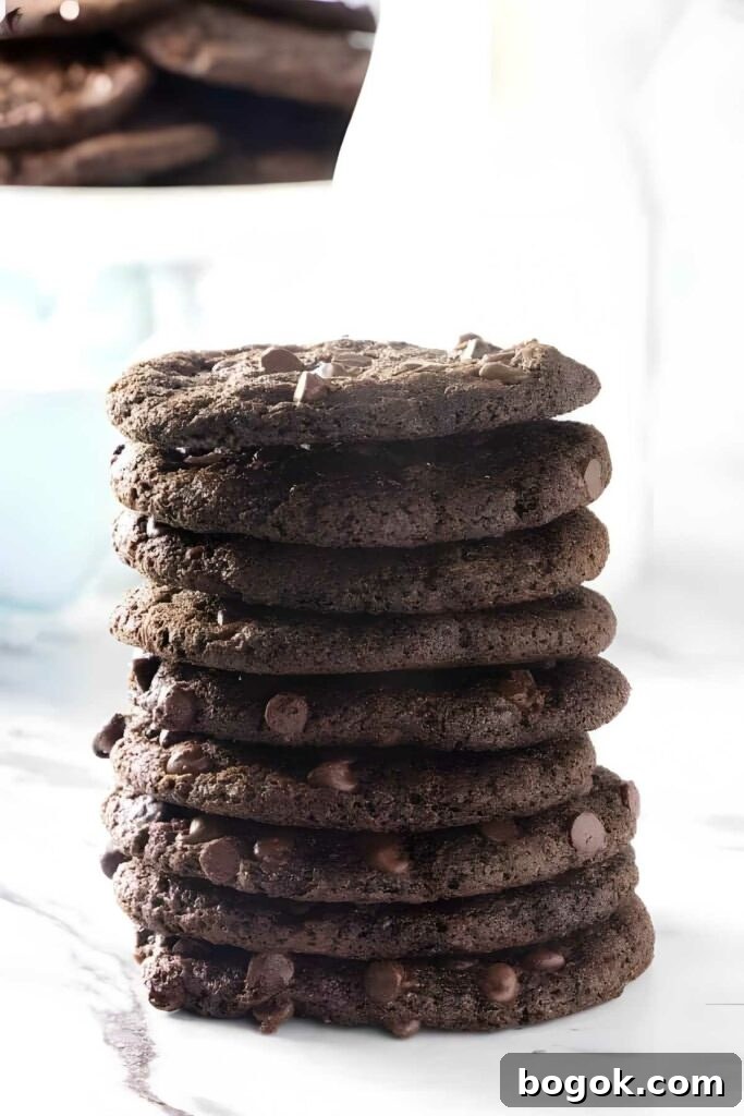 Stack of thin chocolate cookies on marble, blurred cookies behind.