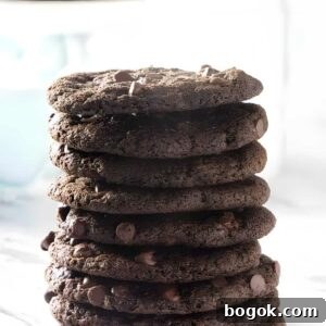 Stack of thin chocolate cookies on marble, blurred cookies behind.