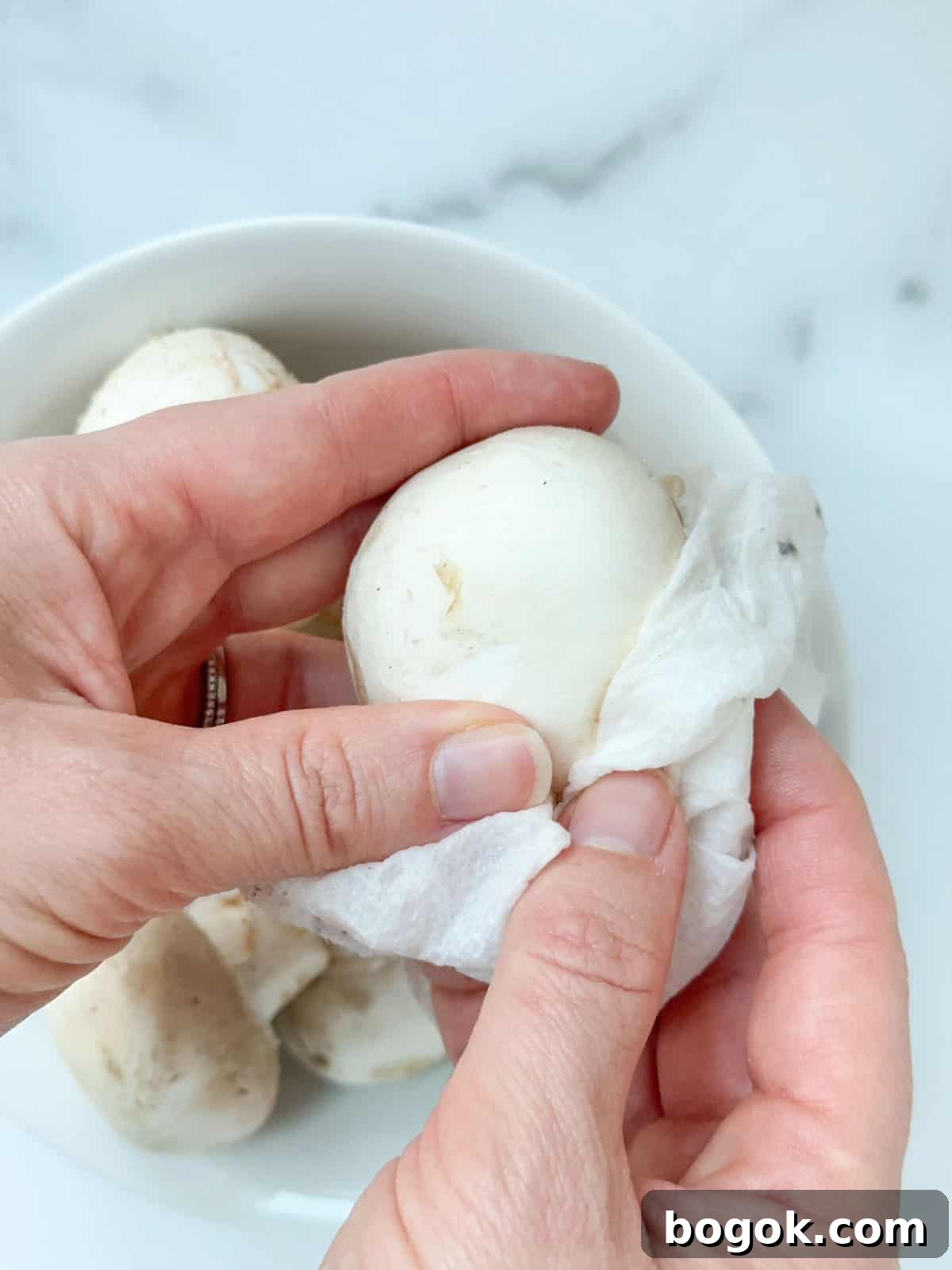 Boursin-Stuffed Mushrooms with Garlic and Herbs 4 A hand wiping off dirt from a mushroom cap.