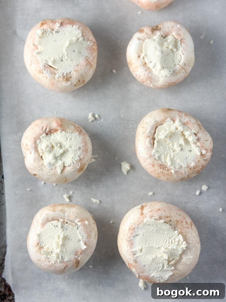 Boursin-Stuffed Mushrooms with Garlic and Herbs 6 Stuffing Boursin cheese into mushroom caps on a baking sheet with parchment paper.