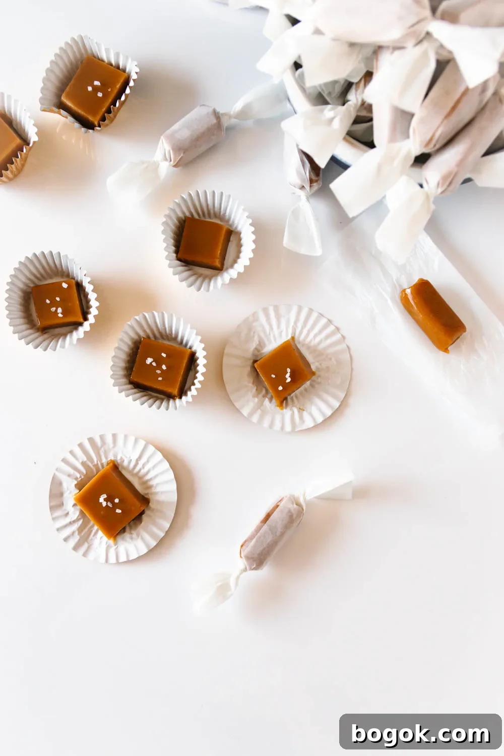 Creamy Goat Milk Caramels: Rich Handmade Candy Recipe 4 overhead view of the caramels - some wrapped in wax paper and some sitting in cupcake liners - scattered over a white surface