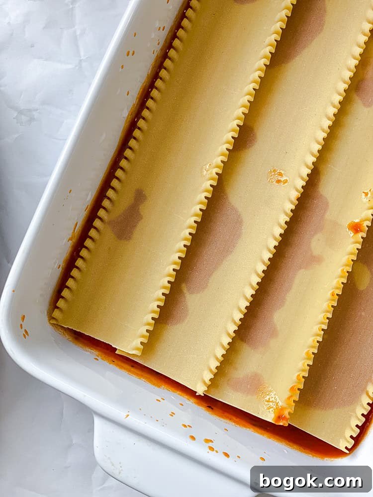 lasagna noodles layered over marinara sauce in a baking dish.